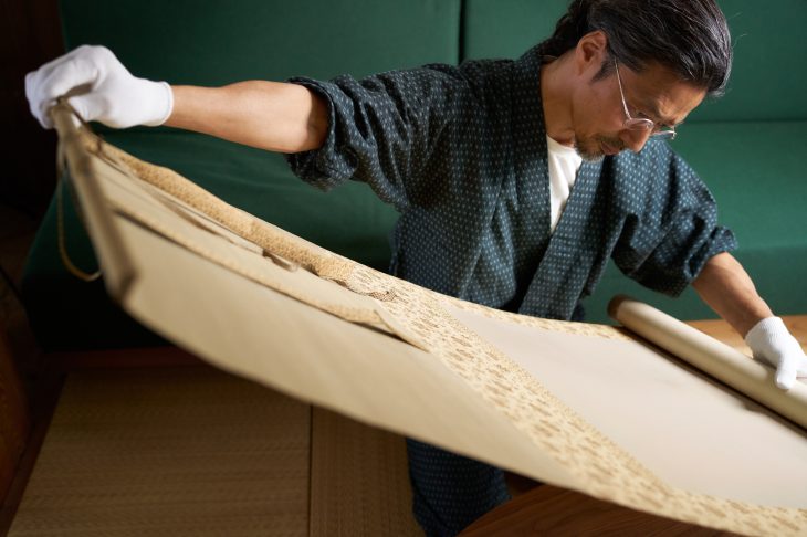 掛け軸を広げてチェックしている人