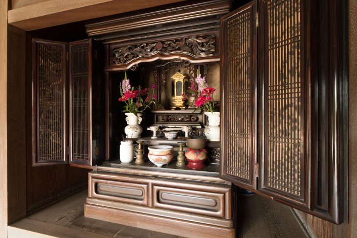 扉が開いた状態で置かれている黒檀風の仏壇にお鈴や花台など全てがセットされている写真