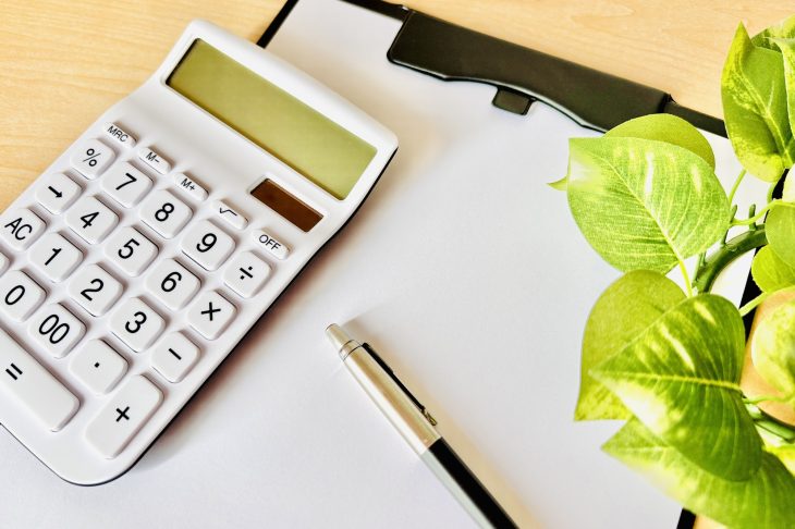 机の上に電卓とドキュメントフォルダー、ペンが並べられている写真