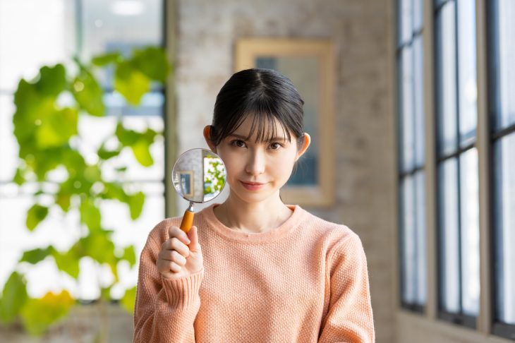 虫眼鏡を持つセーターを着た女性