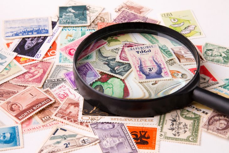 さまざまなデザインの切手の上に、ルーペが乗せられている写真