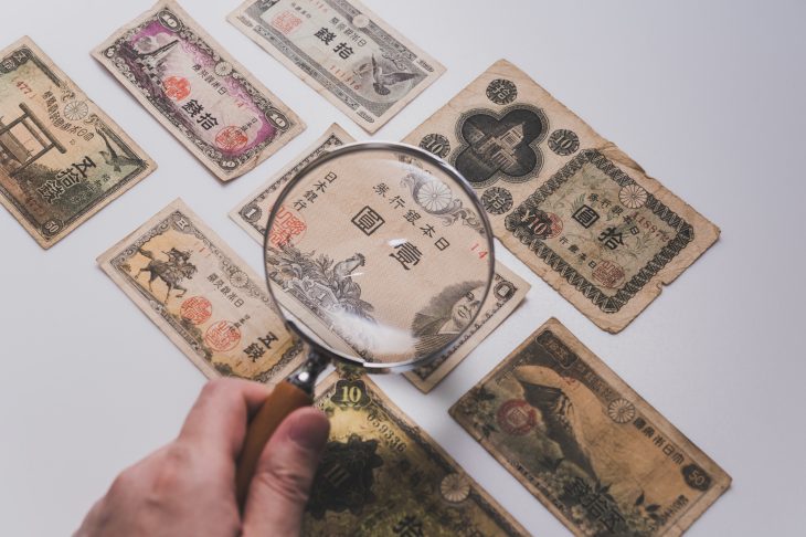 並んでいる古紙幣をルーペで確認している人