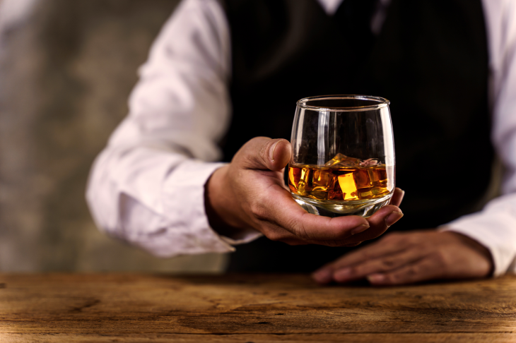 グラスに注がれたウイスキーを渡すバーテンダー