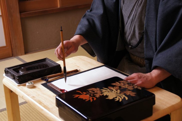 右手に筆を持ち、書き始める和服姿の男性