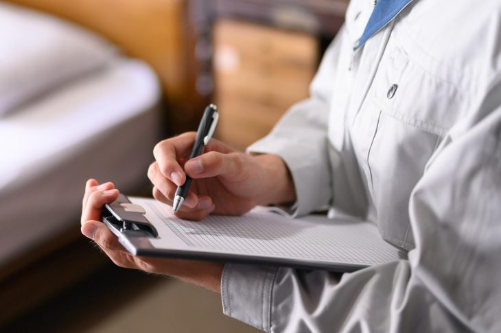 作業服を着た男性がクリップボードに挟んだ紙に何か書いている写真