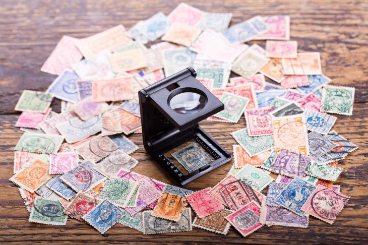 木製の台の上に乱雑に並べられた使用済み切手とルーペの写真