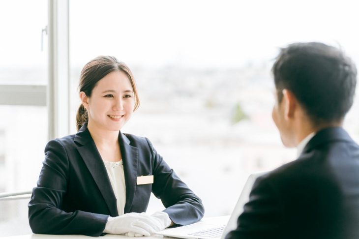 男性と向かい合って座り、笑顔で話す白い手袋をした女性