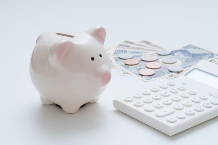 陶器製の豚の貯金箱と電卓、お金が並んでいる写真