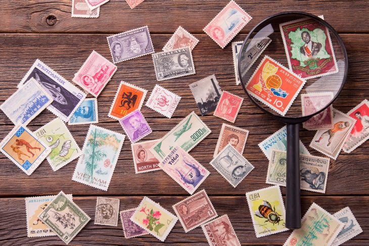 木製のテーブルの上にバラの切手と虫眼鏡が並んでいる写真