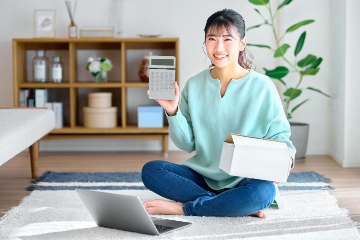 部屋で計算機を見ながら荷物を確認する若い女性