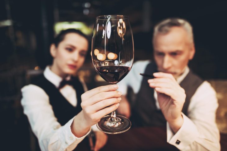 グラスに注がれた赤ワインの様子を観察する男女