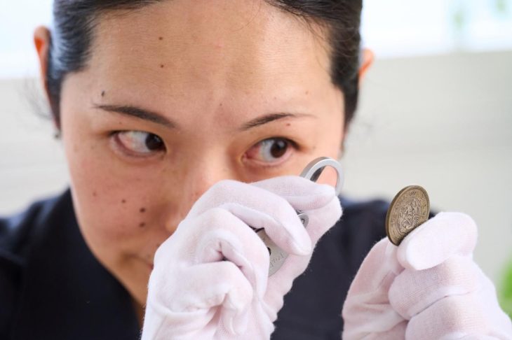 古銭をルーペでチェックする査定士風の女性