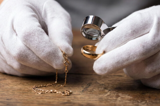 白手袋をしたプロの査定士が、ルーペを使って金メッキジュエリーの刻印を検査している手元のクローズアップ写真