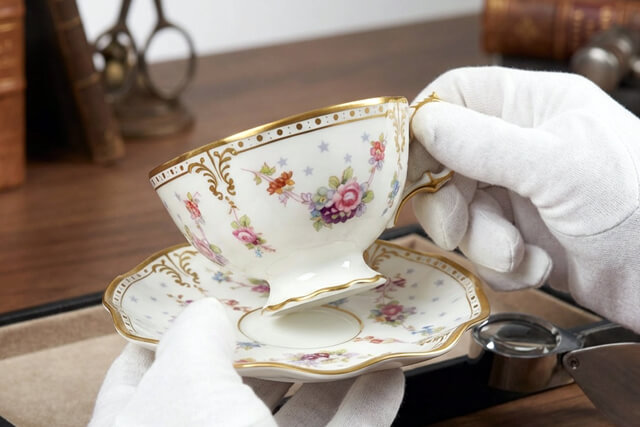 専門の査定士が白手袋を着用し、ロイヤルクラウンダービーのカップ＆ソーサーを丁寧に査定している様子