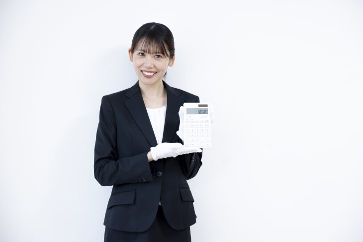 白い手袋をはめて電卓を持っている笑顔の女性