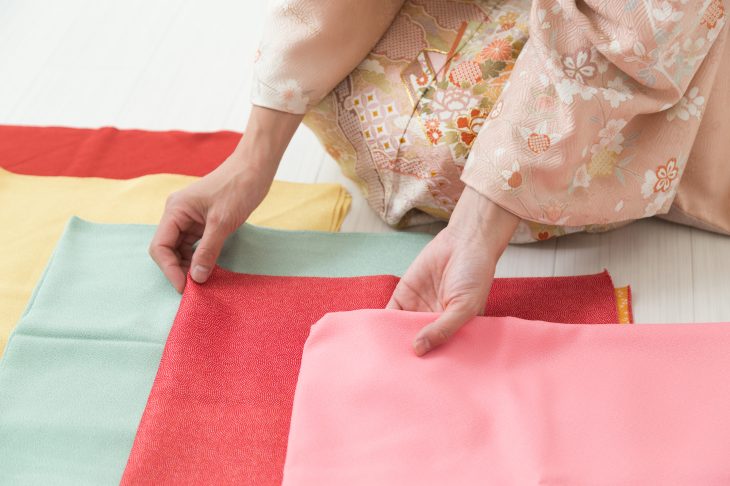 床に広げた生地を触っている女性の手元が写っている写真