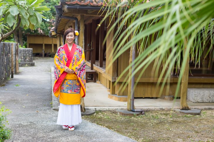 建物の前に立っている紅型を着用した女性