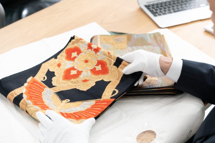 白い手袋をはめて帯に触れる人の手元