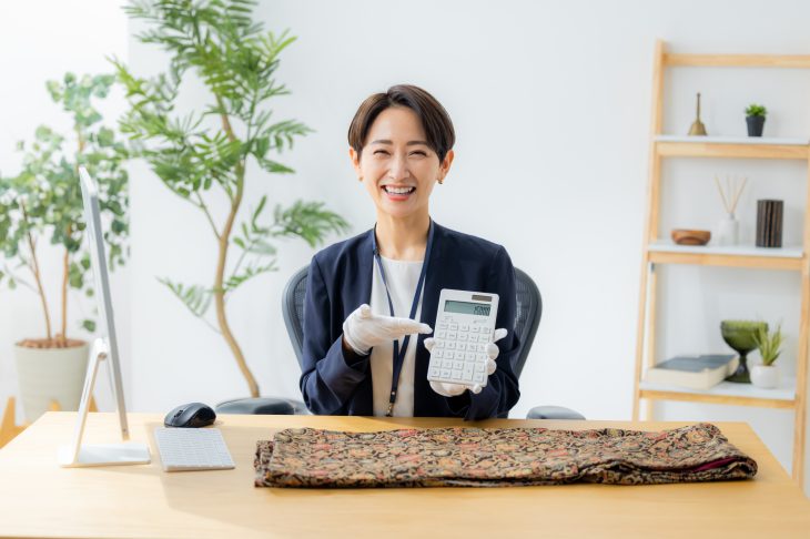 電卓の数字を見せる白い手袋をはめた笑顔の女性