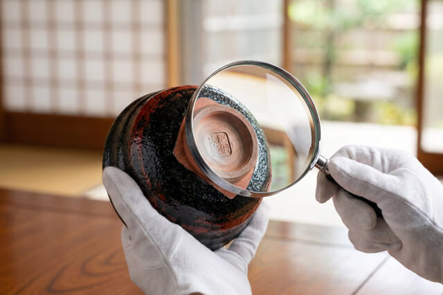 白い手袋をしたプロの査定士が茶道具（茶碗）を丁寧に鑑定している様子｜骨董買取のイメージ