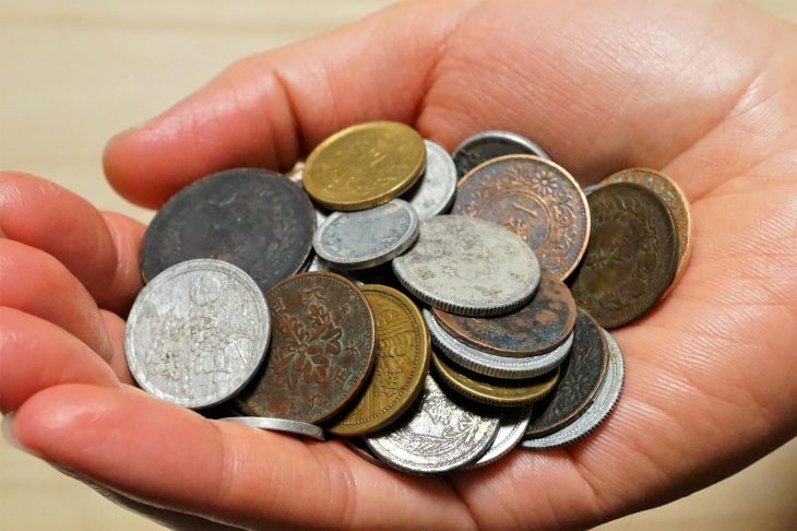 片手の手のひらに一銭硬貨などの古銭を十数枚載せて持っている写真