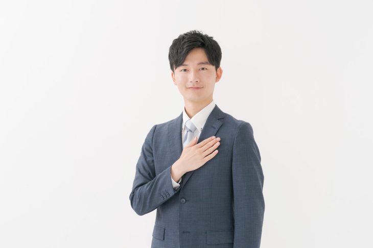スーツ姿で右手を胸に当てる男性