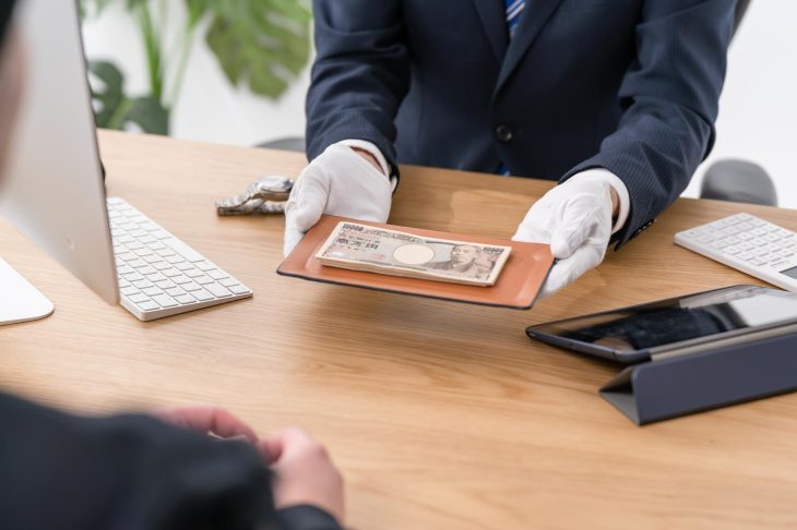 一万円札が数枚載っているトレイを持って差し出している手元の写真