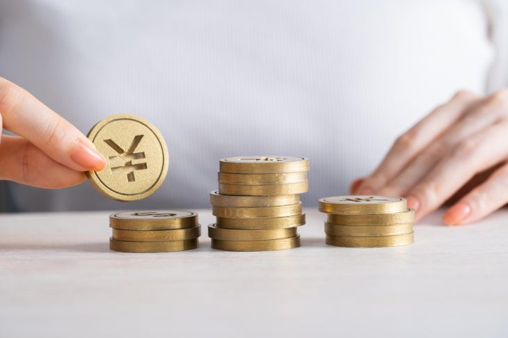 机の上に積まれた金貨を1枚つまみ上げる手元