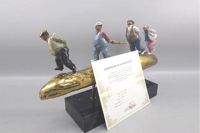 金色の棒の上に人物が並んだ立体作品と前に立てかけられた証明書