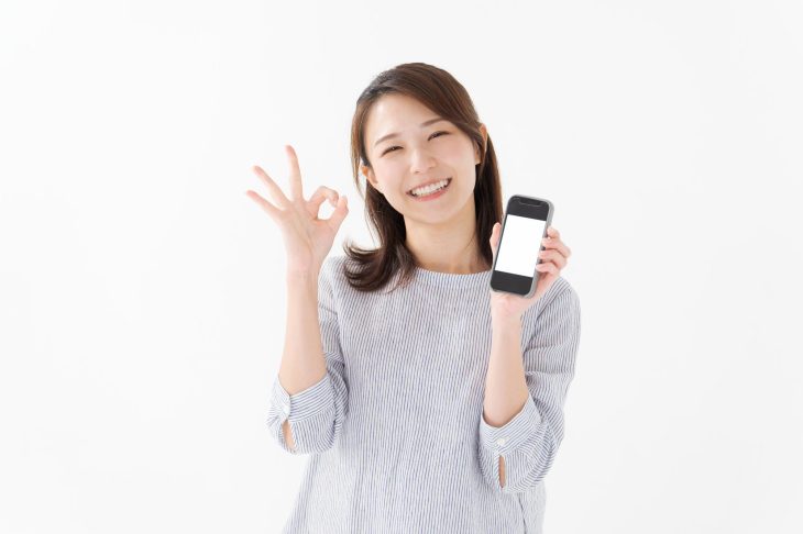 スマートフォンを持ってOKサインを出す女性