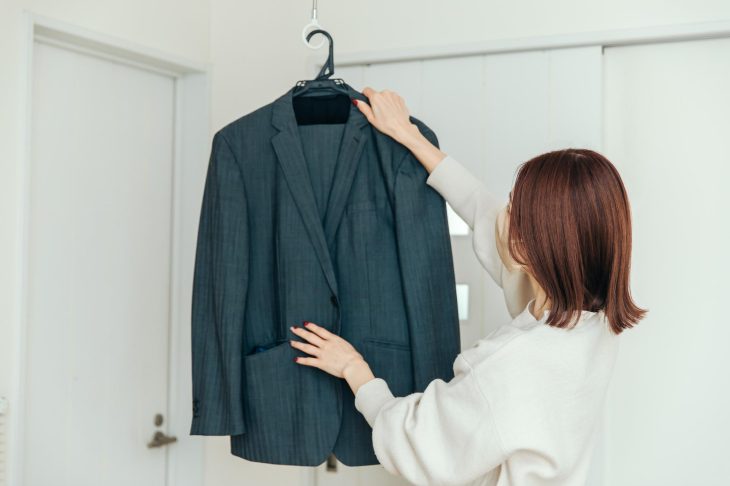 ハンガーにかかったグレーのスーツを見ている女性の後ろ姿