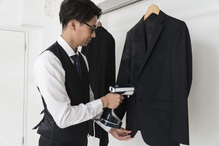 ダークカラーのスーツにアイロンをかけている眼鏡をかけた男性