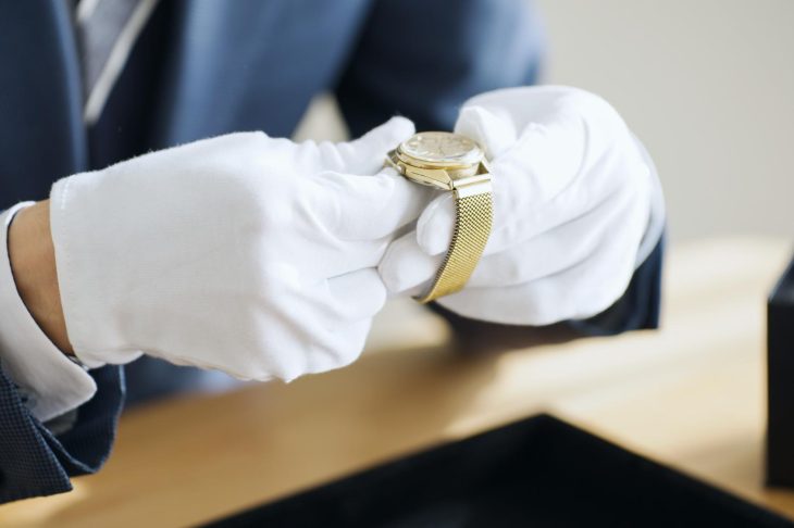 手袋をした人物が金色の腕時計を手に取り、状態を確認している様子