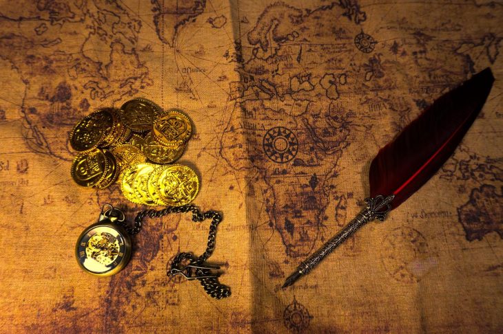 古地図の上に置かれた金貨や懐中時計、羽根ペン