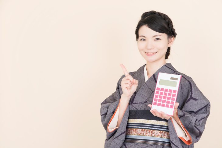 電卓を持って人さし指を立てる着物を着た女性
