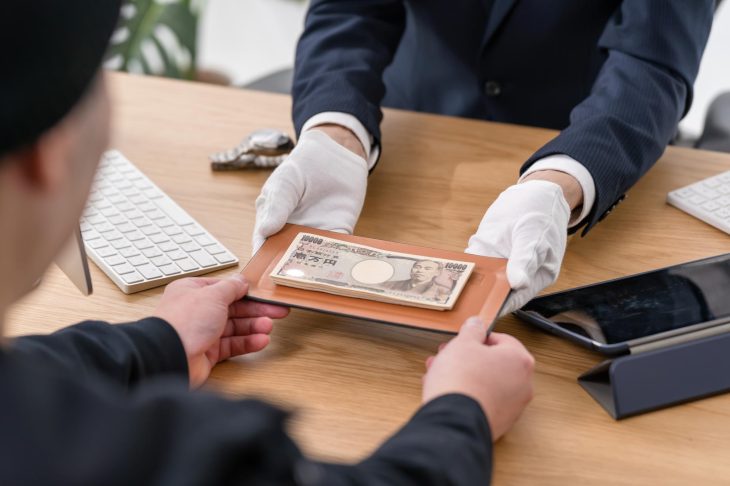 手袋をした人物が机の上で現金を差し出し、受け渡ししている様子
