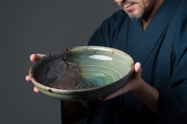 緑色の大皿を両手で持つ和装姿の人物の手元