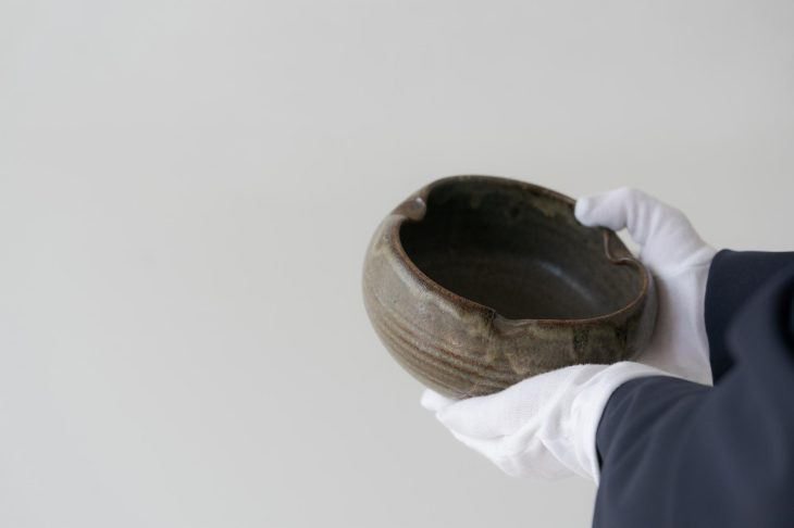 手袋をした人物が陶器の鉢を両手で持ち、状態を確認している様子