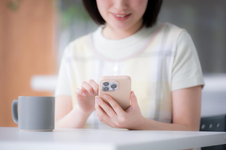 マグカップを置いたテーブルの前で、スマホを操作する女性