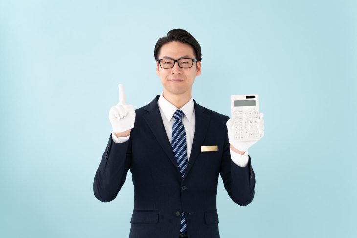 計算機を持って人さし指を立てるスーツ姿の男性