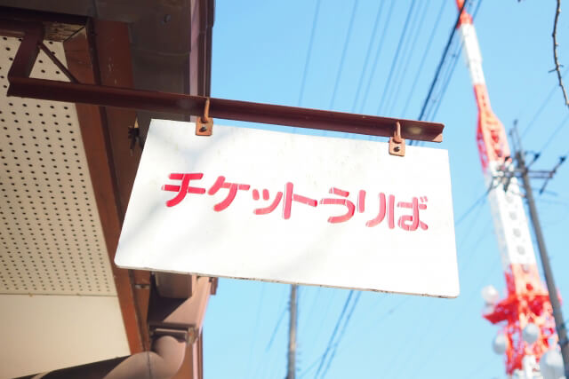 青空と赤白のタワーを背景にした、赤文字で「チケットうりば」と書かれた白い看板