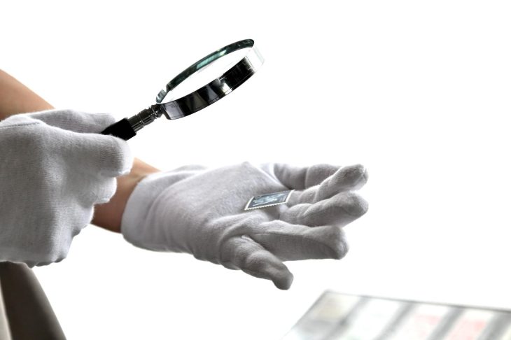 白手袋を着用した人物が、虫眼鏡で切手を鑑定する様子
