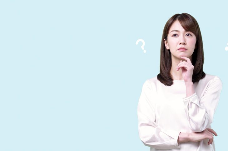 水色の背景で疑問符の横に立つ白い服の女性