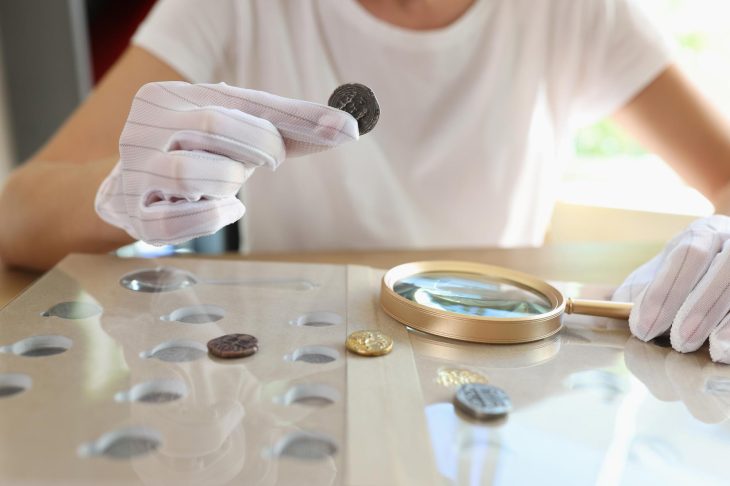 白手袋でルーペを持ち、コインを鑑定・確認する様子