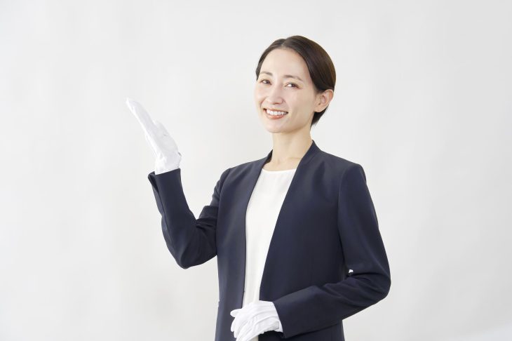 白い手袋をはめた手を挙げて、笑顔を見せる女性査定士