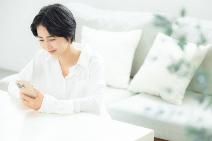 白を基調とした部屋で、スマホを笑顔で見つめる女性