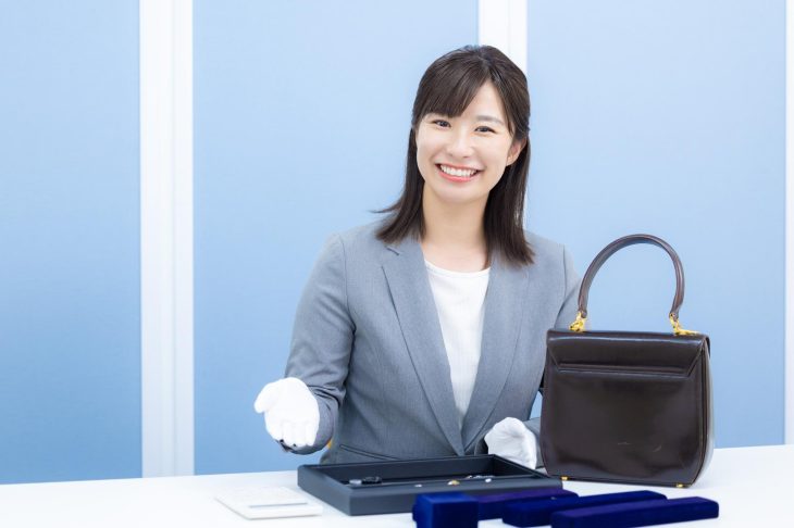 バッグや貴金属を前に笑顔を見せる女性査定士