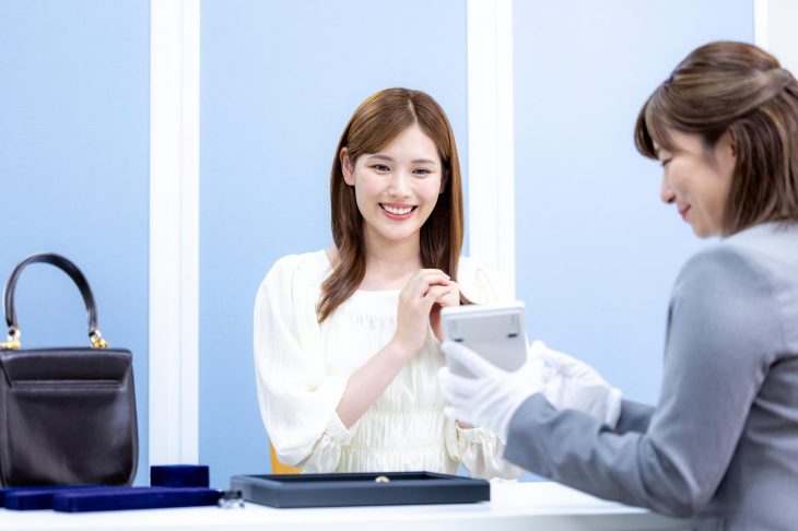 バッグとアクセサリーの査定額を提示する査定士と笑顔の女性客
