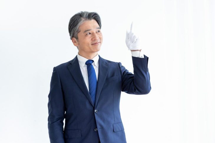 白い手袋をして上を指さすスーツ姿の男性