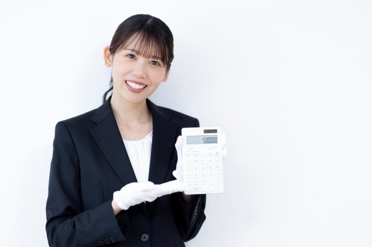 白い手袋をして電卓に表示した金額を見せる笑顔の女性